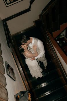 Elegant couple kissing on staircase, captured from above, creating a dramatic and intimate mood.
