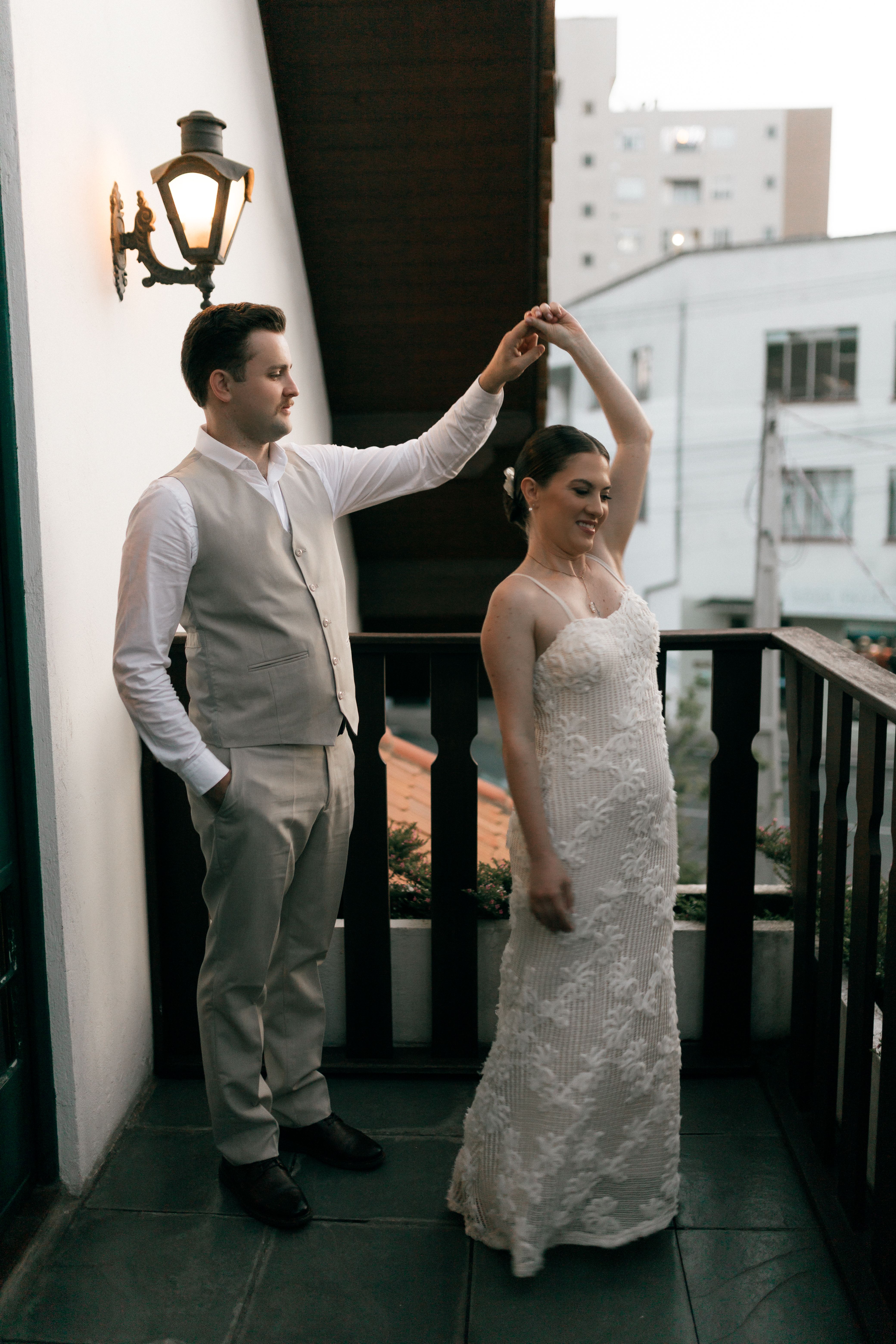 Bride and groom gracefully dance on a balcony adorned with soft evening light.