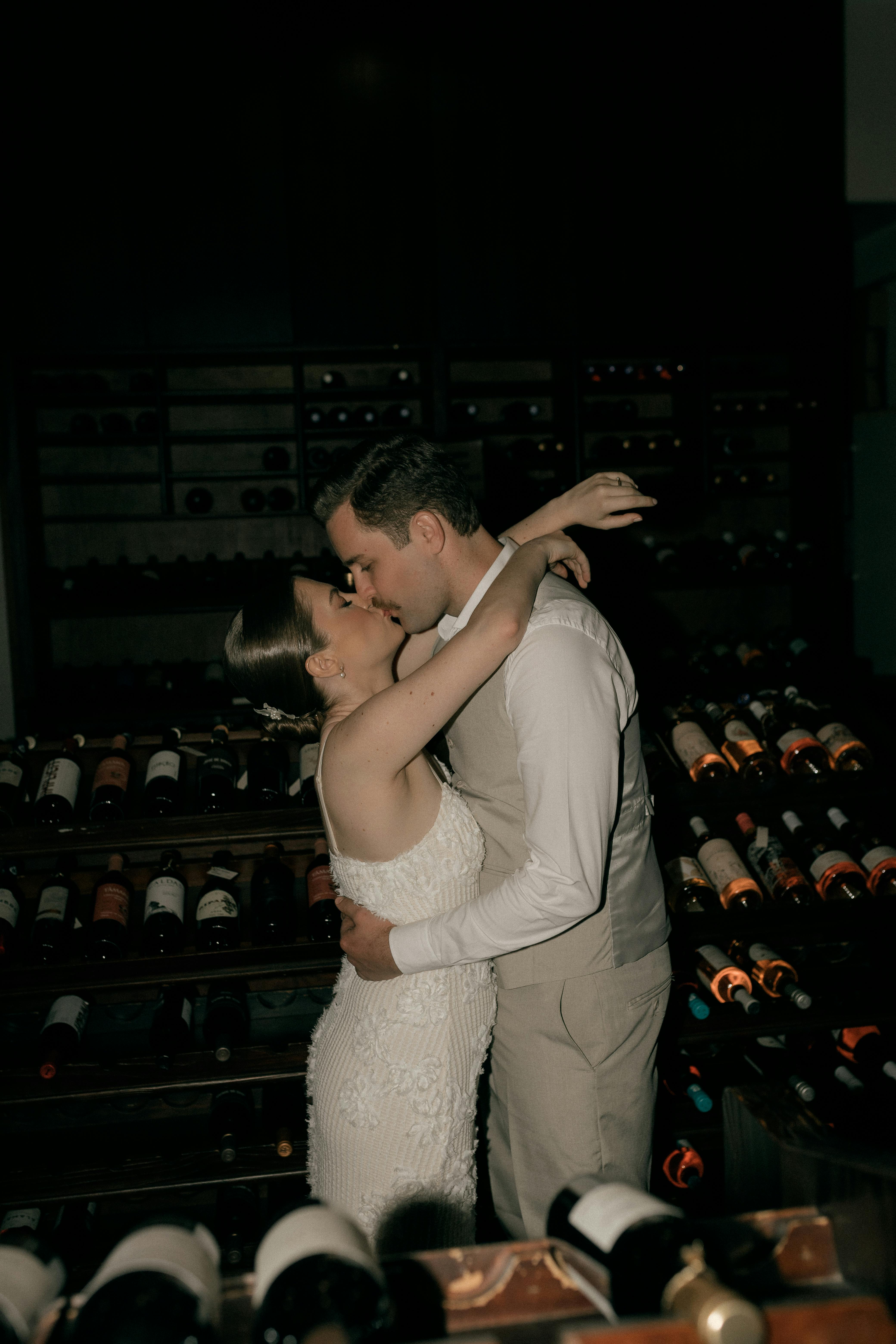 A loving couple shares a tender embrace surrounded by wine bottles.