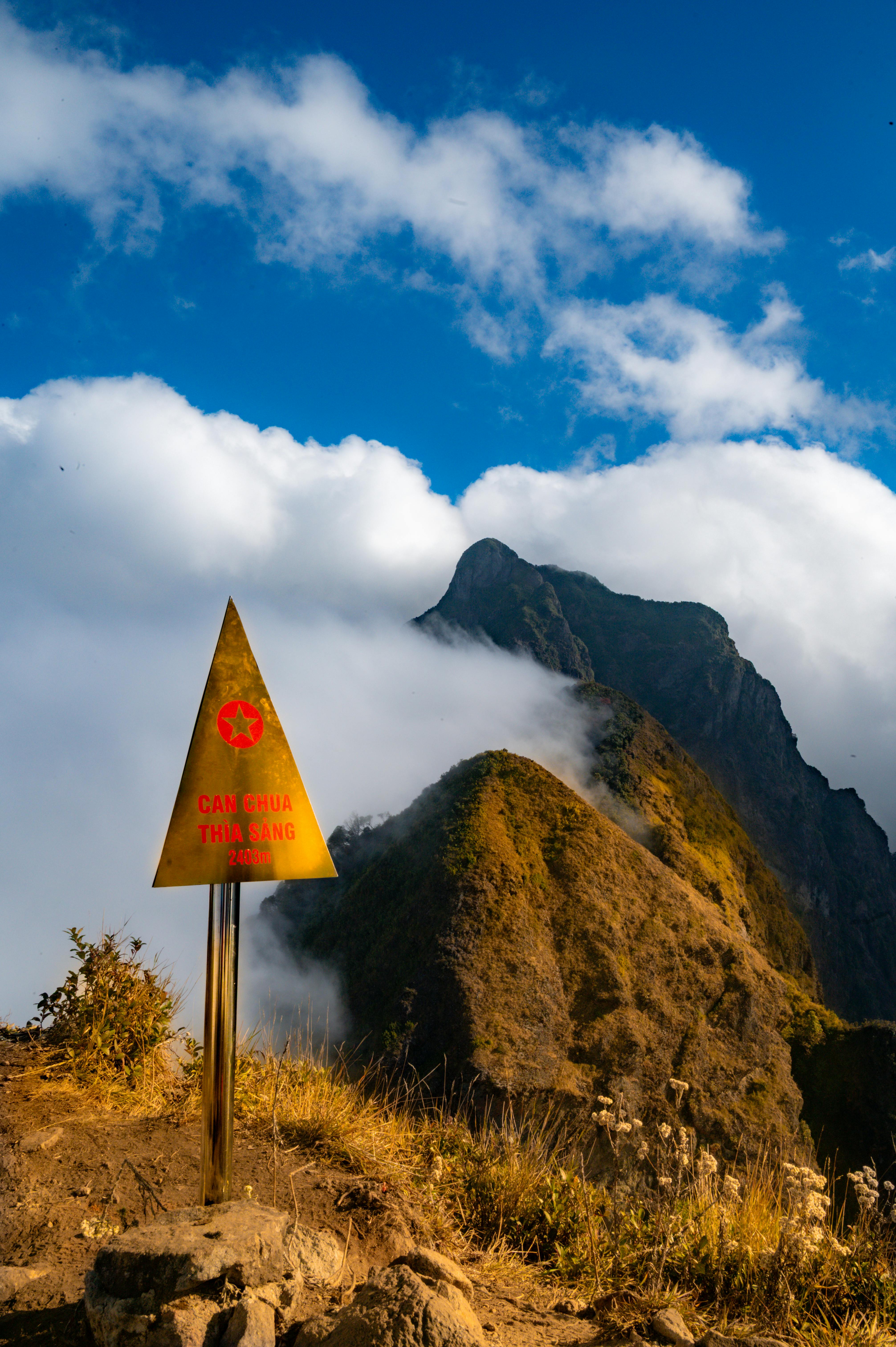 Dramatic mountain landscape with a triangular warning sign, clouds and rugged peaks.