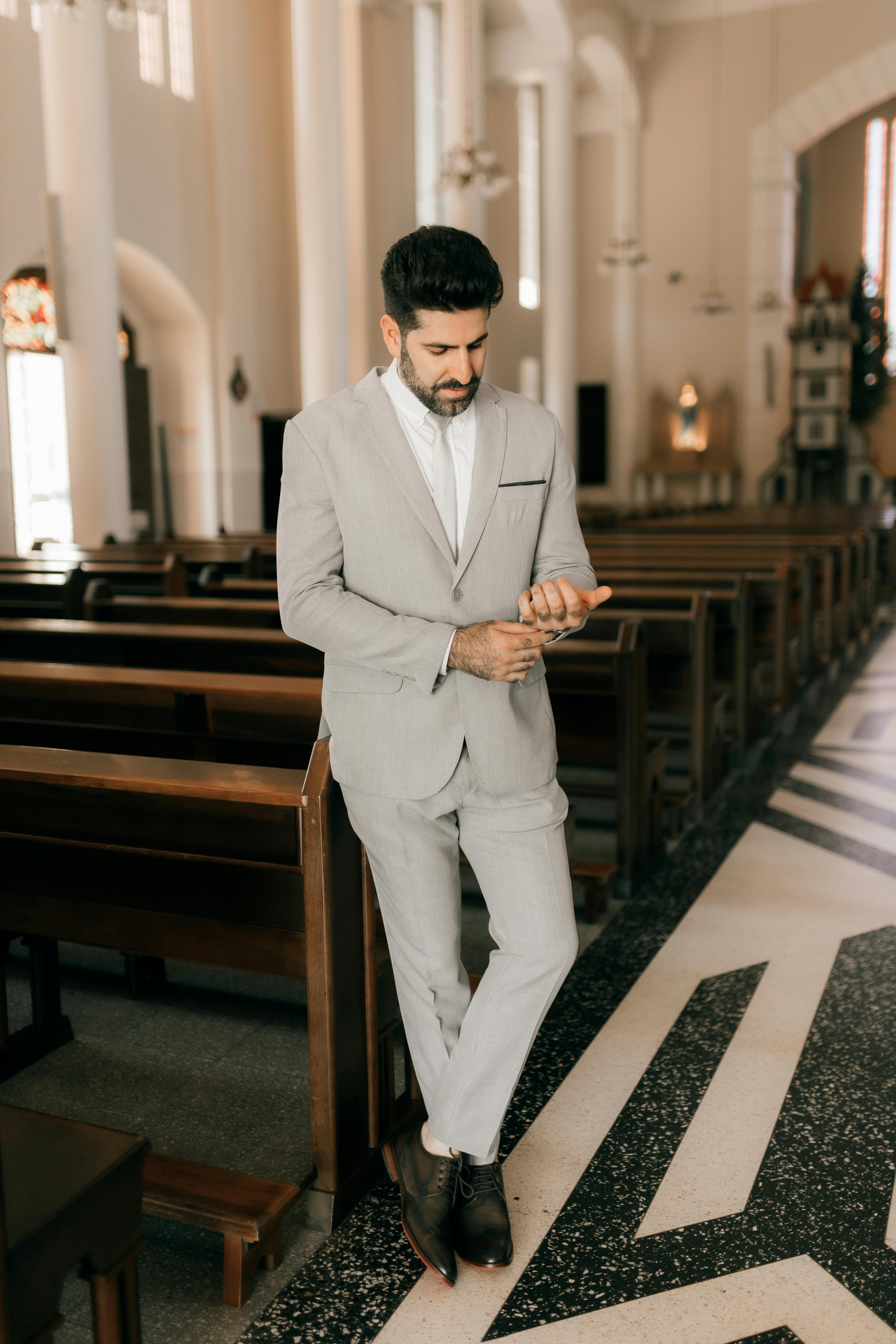 Man in a stylish suit stands in a beautifully designed church interior checking his phone.