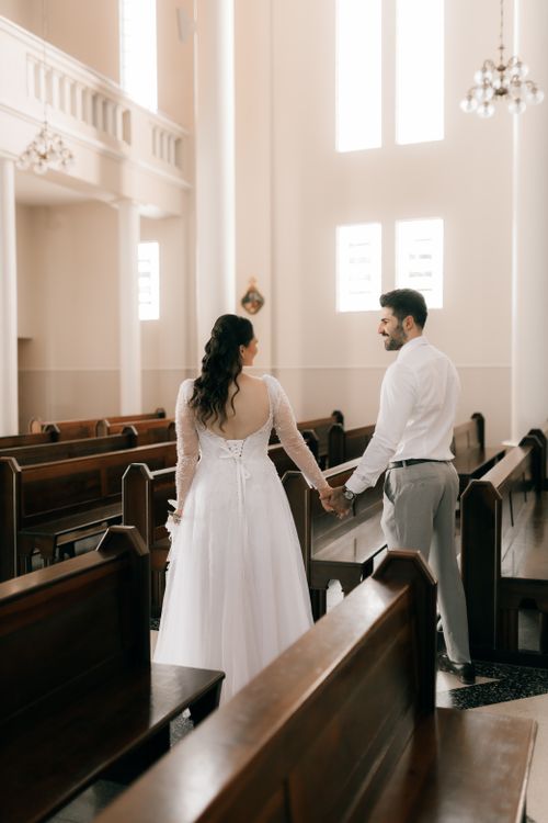 Free Bride and groom holding hands in a beautifully lit church, capturing a loving wedding moment. Stock Photo
