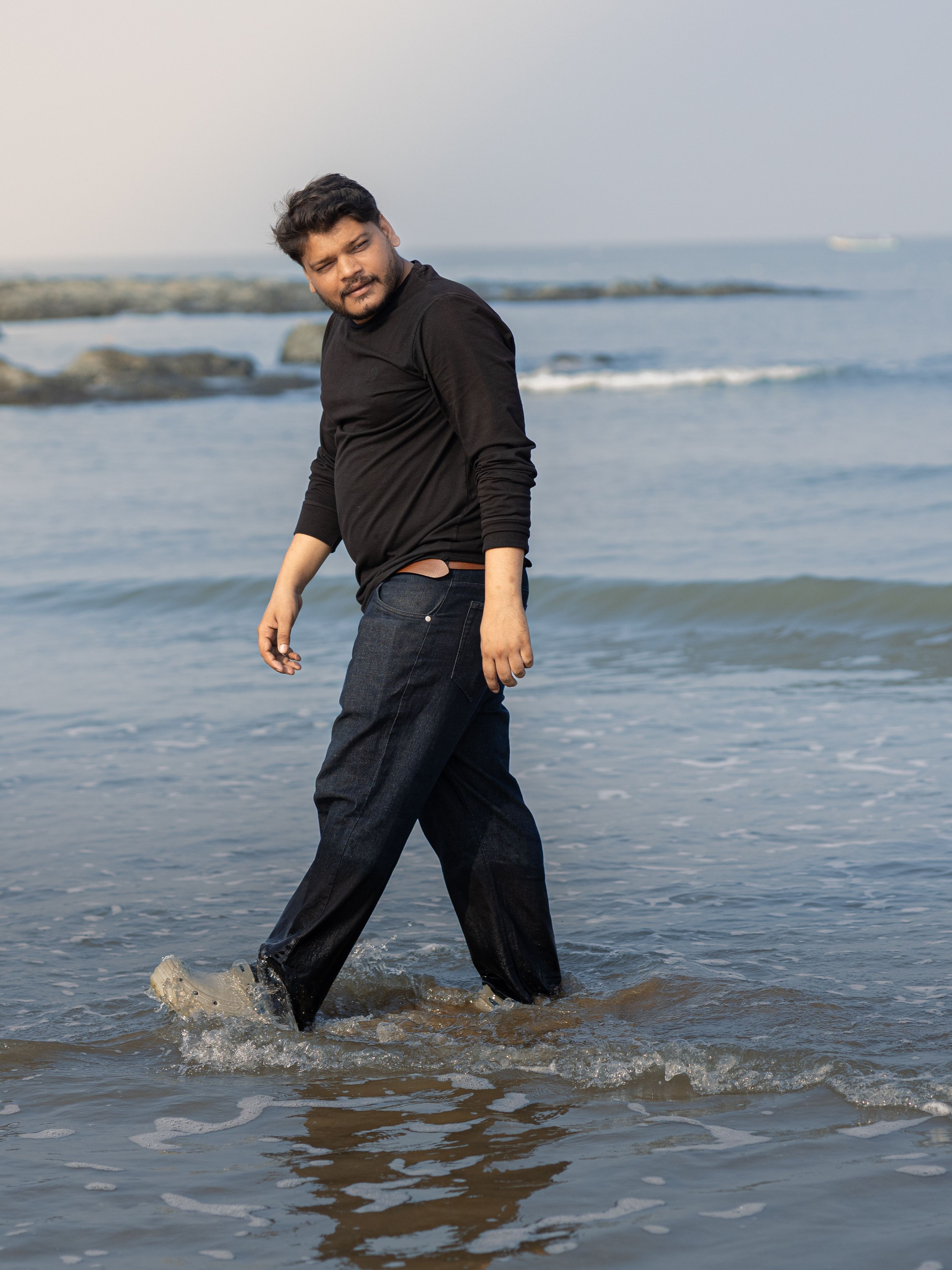 Casual man walking on a beach with waves, exuding confidence and relaxation.