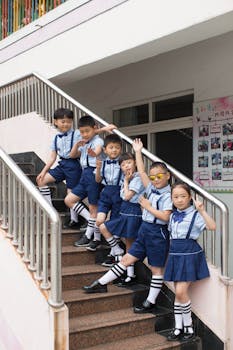 Cheerful schoolchildren in uniforms pose on stairs, outdoors.