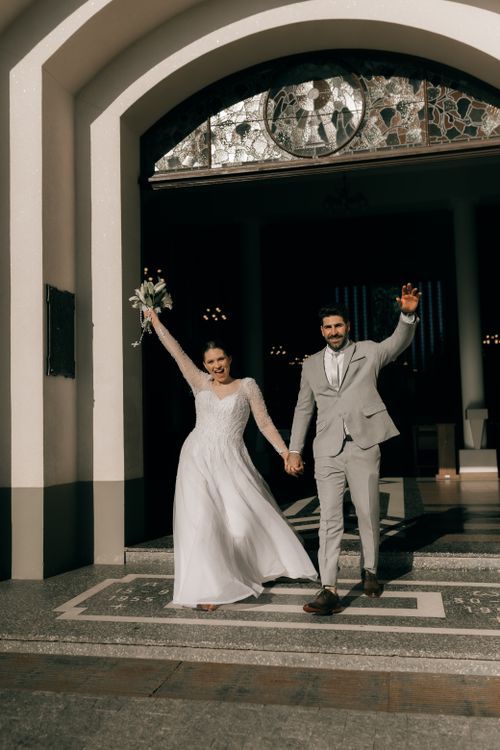 Free A joyful couple exits the church, celebrating their wedding day in sunlight. Stock Photo