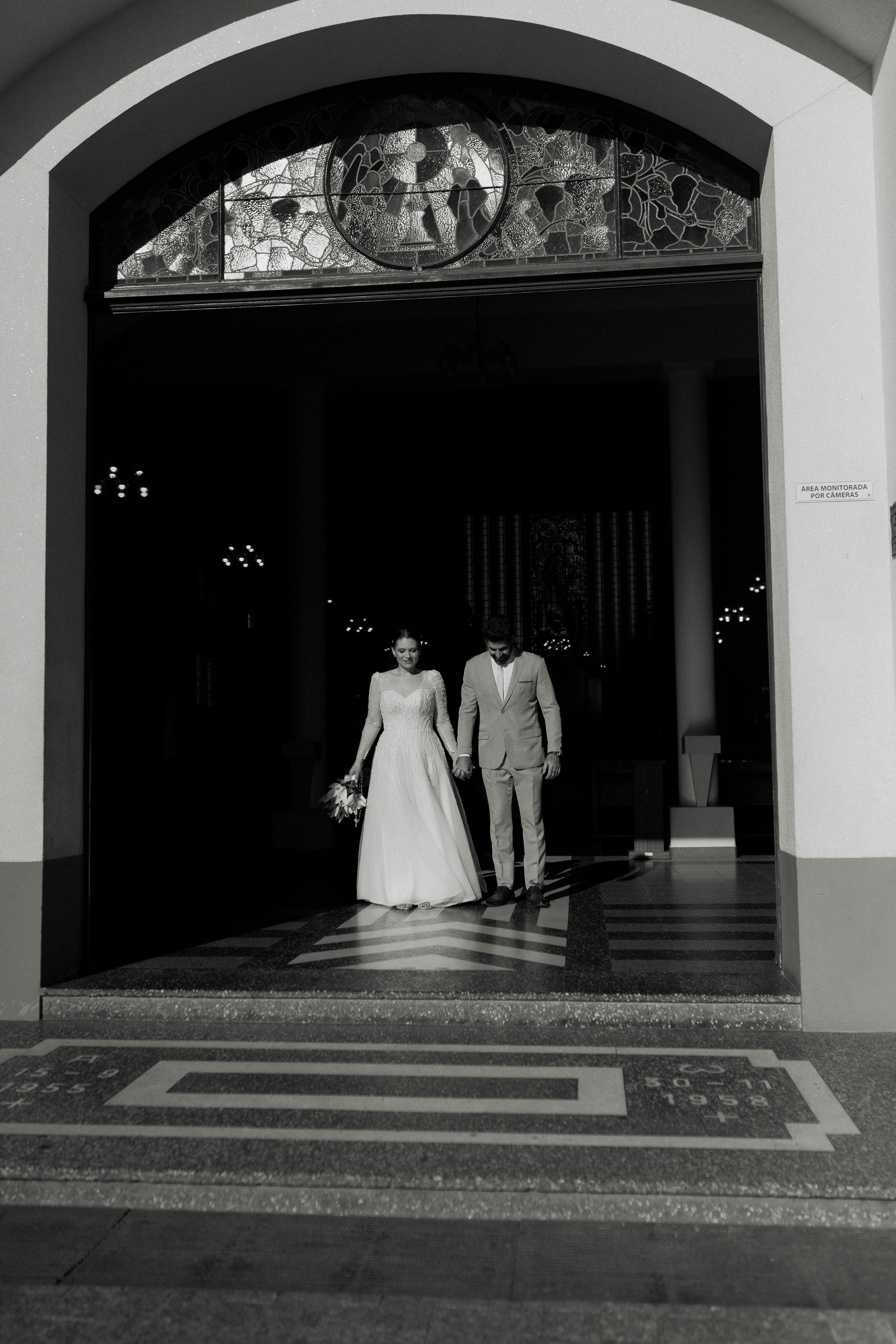 A bride and groom in wedding attire leaving a church, captured in monochrome.