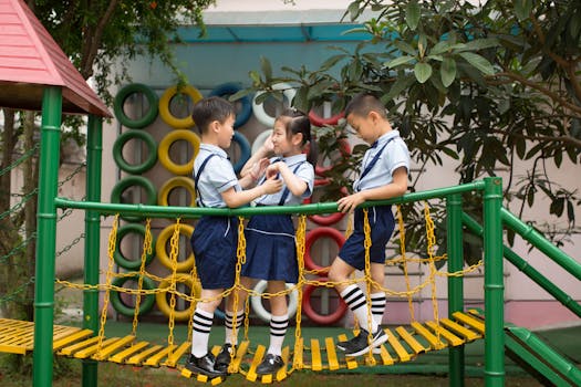 Three children in school uniforms playing on a colorful playground bridge outdoors.