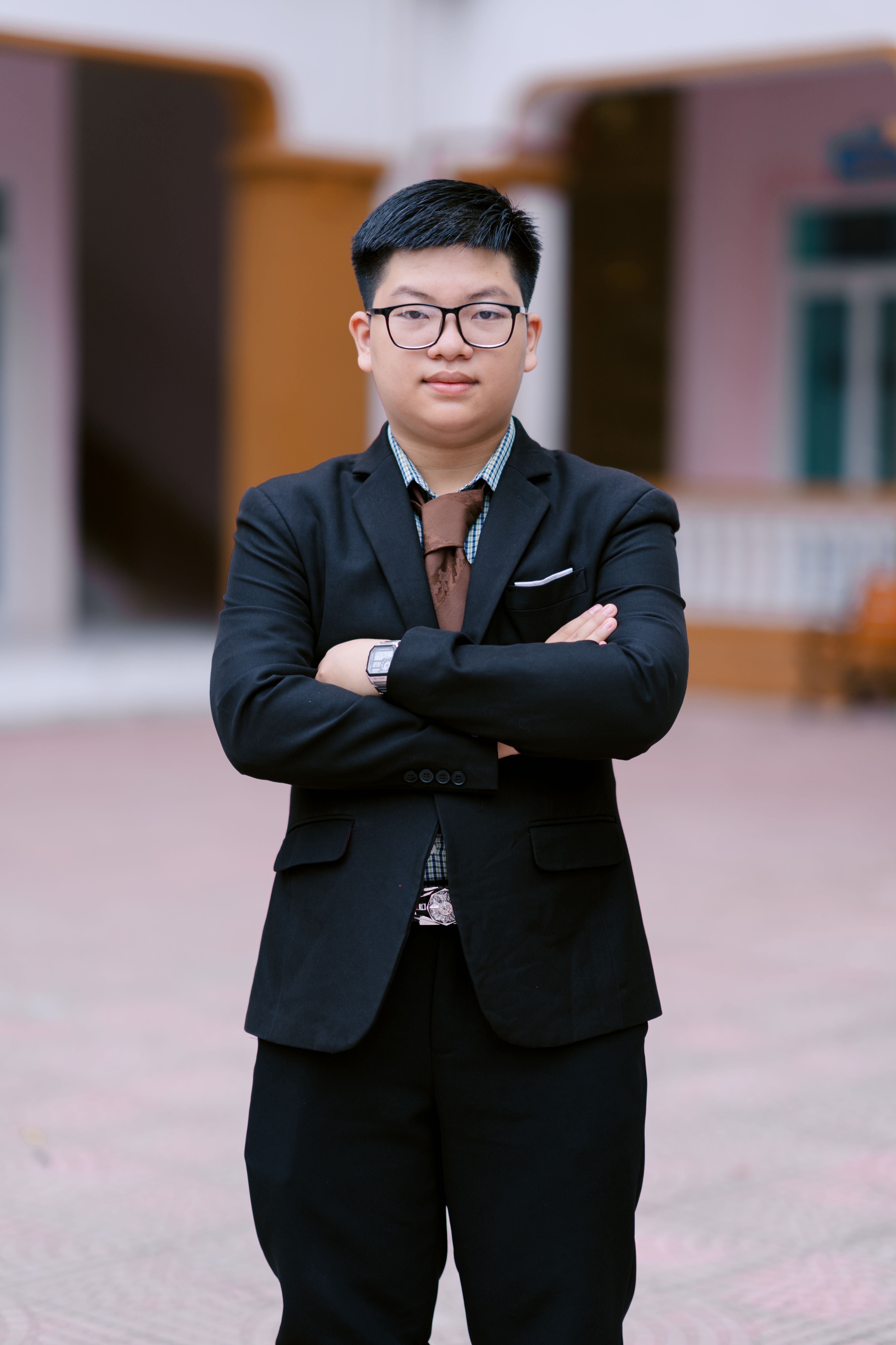 Confident young adult male in a suit standing outdoors with arms crossed, showcasing professionalism.