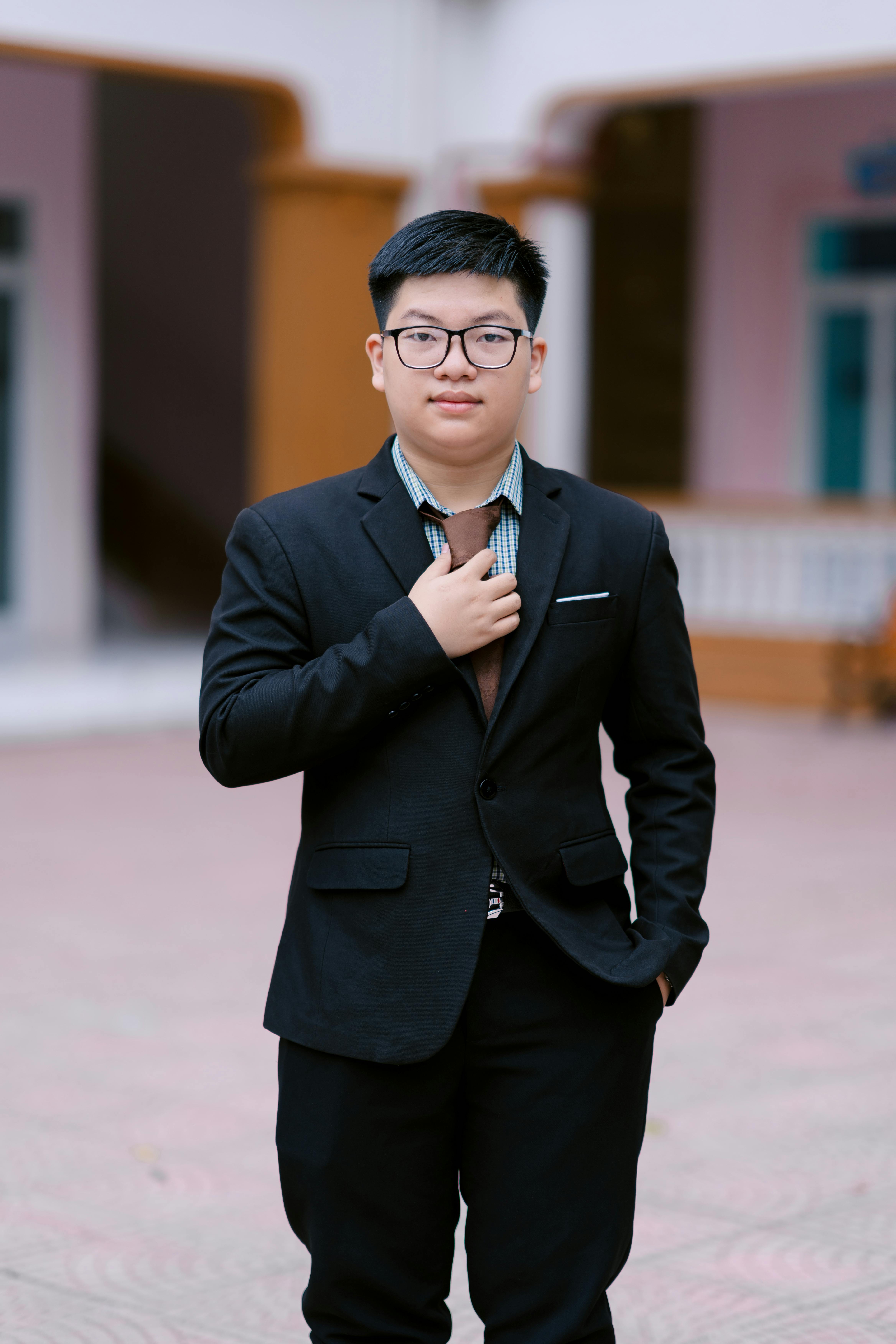 Young adult in suit adjusting tie, standing outdoors in a formal setting.