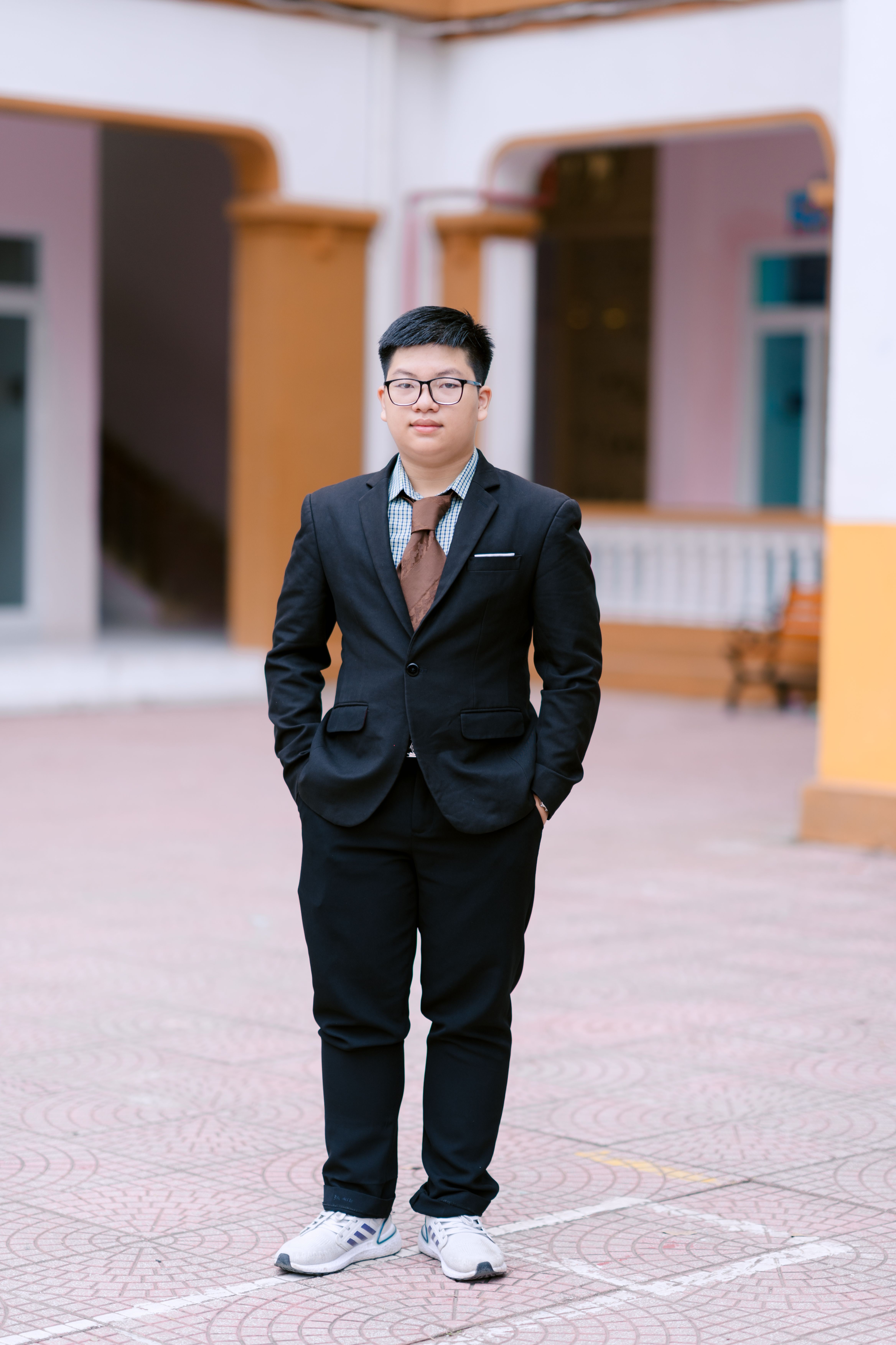 Young man in formal attire standing outside in an open area, hands in pockets.