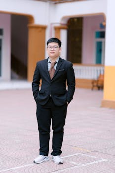 Confident young adult in a suit and sneakers standing outside a building.