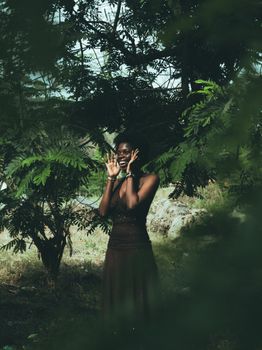 A woman joyfully poses amidst lush green trees, expressing happiness.