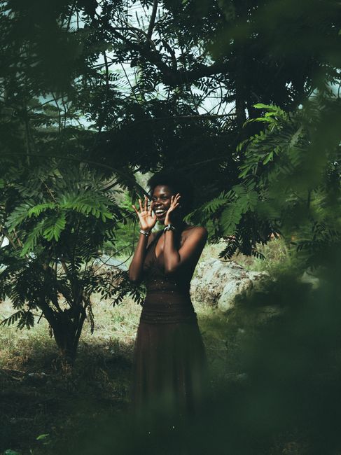 A woman joyfully poses amidst lush green trees, expressing happiness.