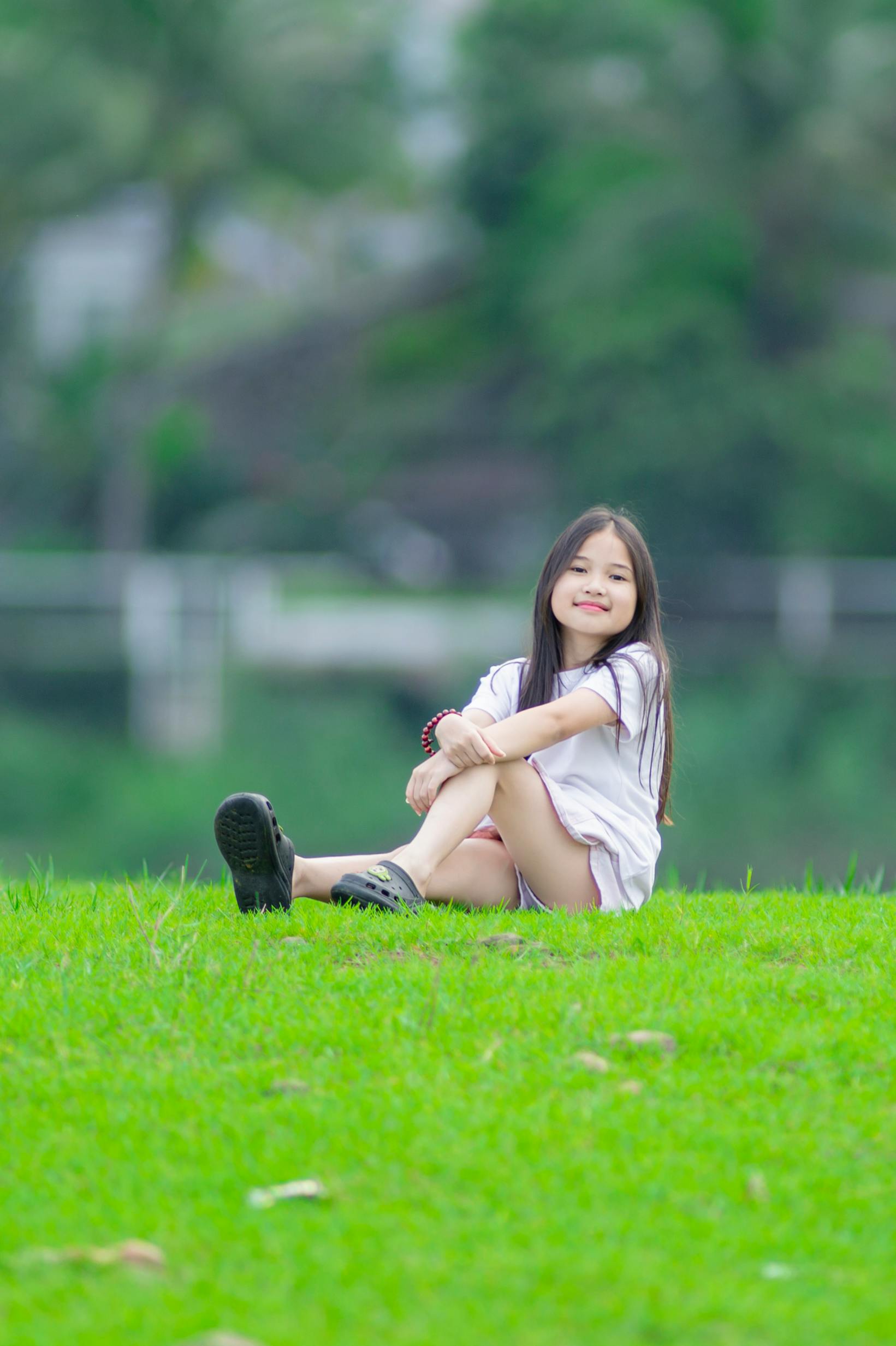 Gratis Gadis muda yang gembira menikmati hari yang cerah di halaman rumput hijau yang subur di Hanoi, Vietnam. Foto Stok