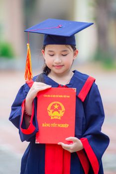 A young girl in graduation attire holding a diploma, signifying educational achievement in Vietnam.