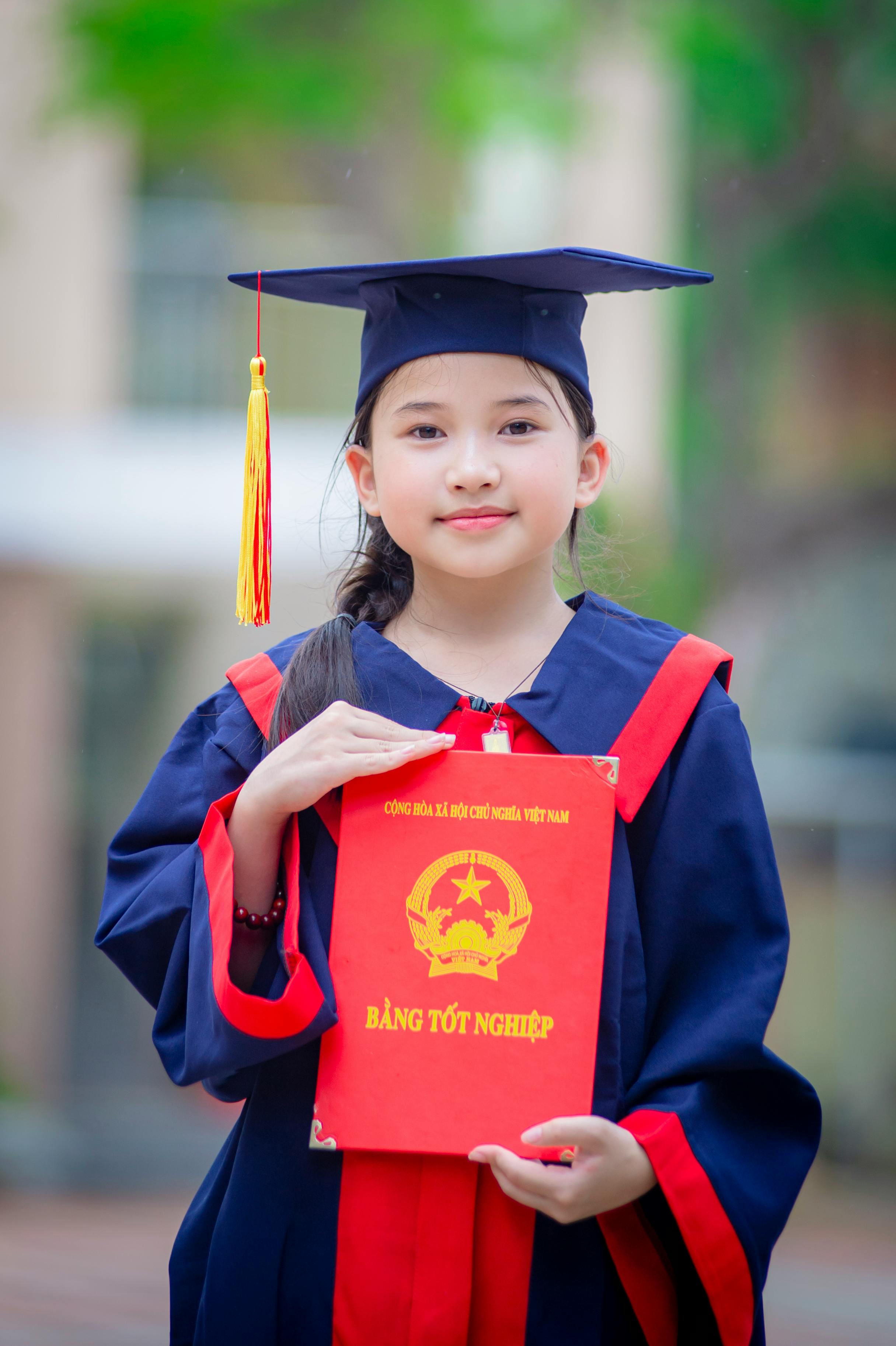 gratis Een jong meisje poseert trots in haar afstudeerkleding met haar diploma in Hanoi, Vietnam. Stockfoto