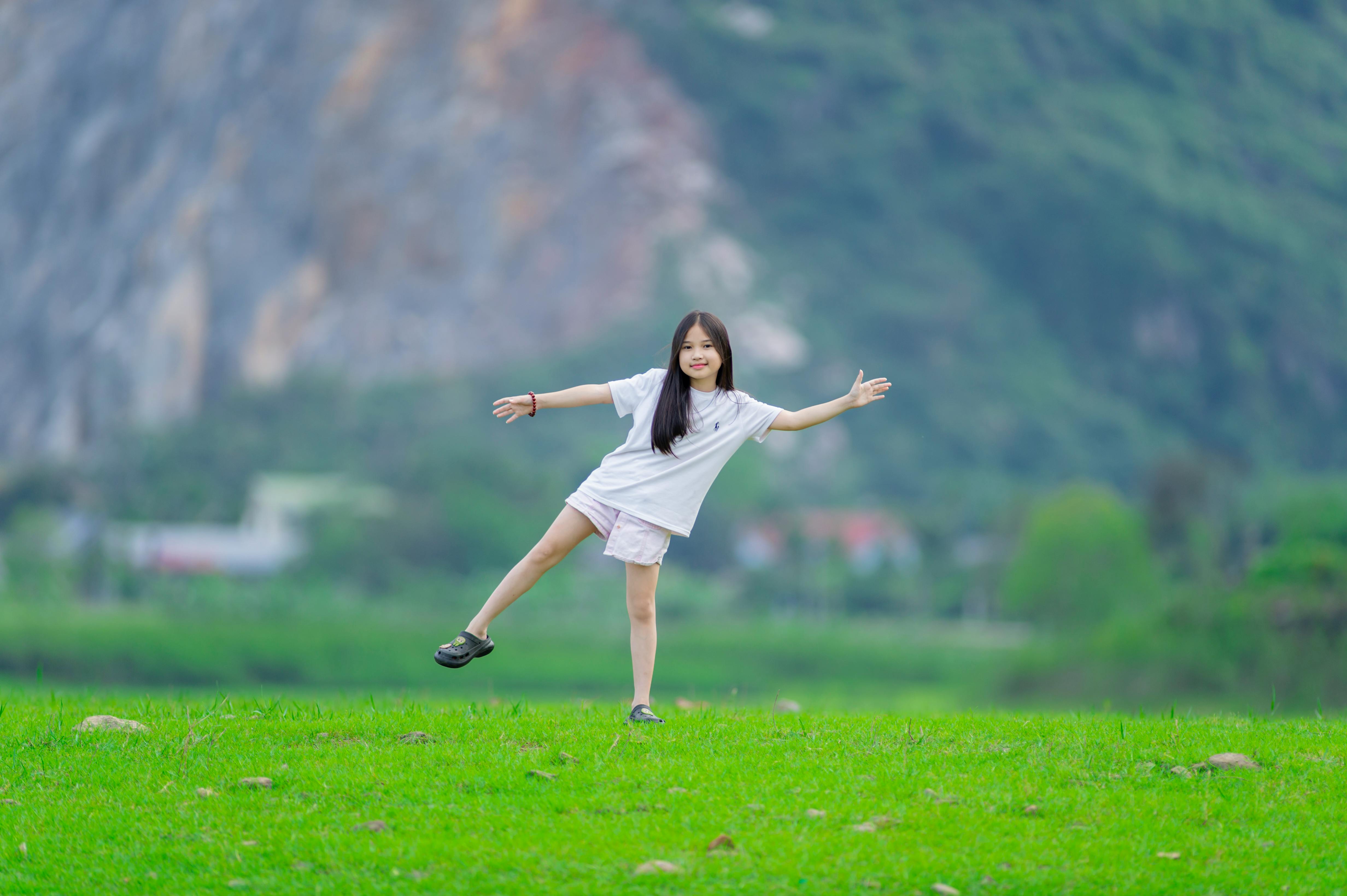 gratis Een jong meisje speelt graag op een weelderig groen gazon met majestueuze bergen op de achtergrond. Stockfoto