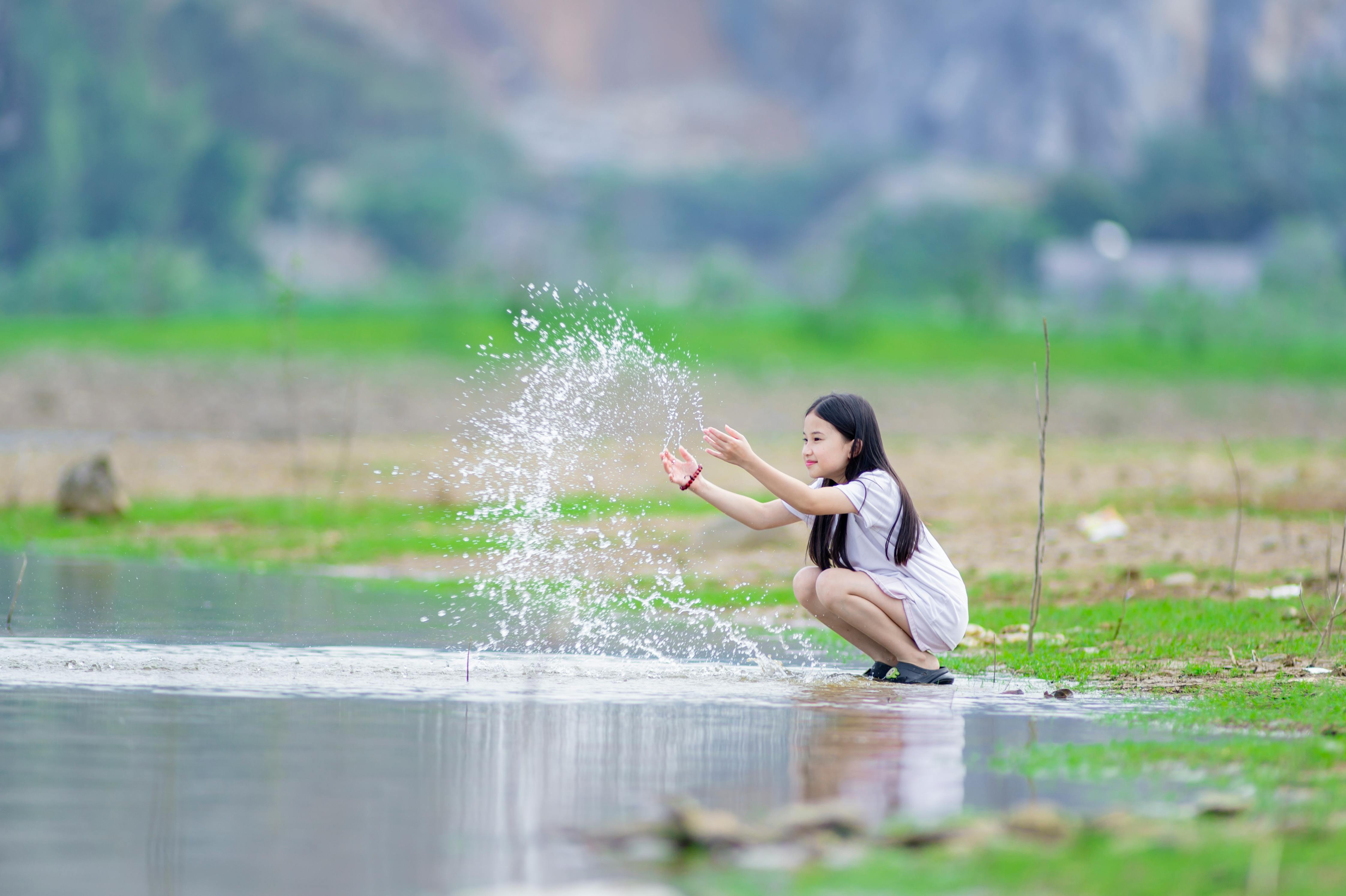 gratis Een vrolijk kind dat in een vijver in Hanoi met water speelt, legt de essentie van speelse onschuld in de buitenlucht vast. Stockfoto