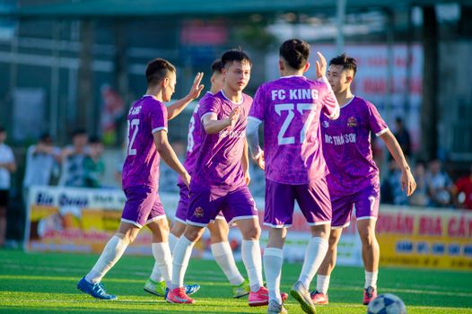 Team of young players celebrating a goal on an outdoor football field in Hanoi, Vietnam.