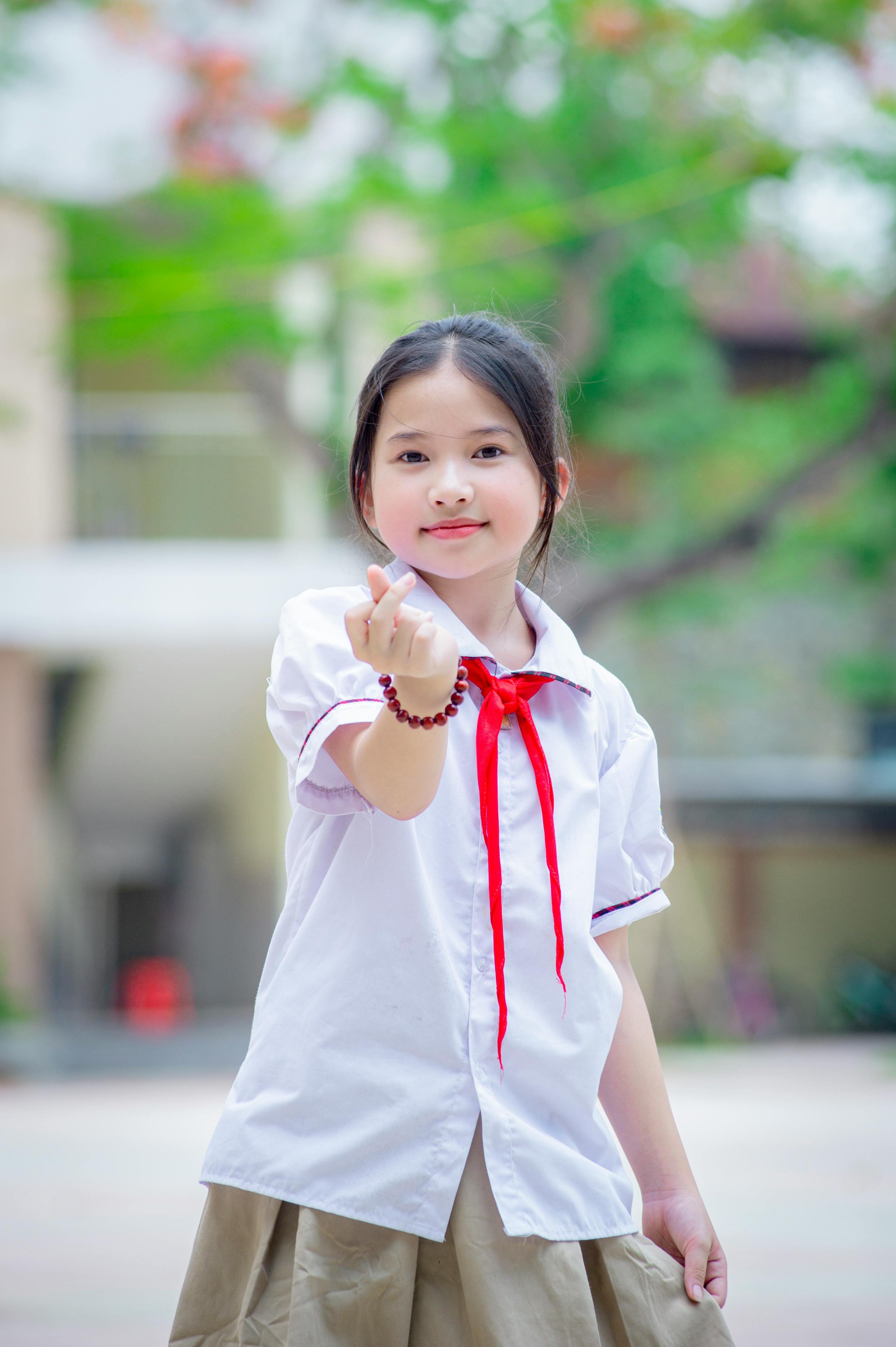 gratis Vrolijk Vietnamees schoolmeisje maakt een hartgebaar in een levendige buitenomgeving in Hanoi. Stockfoto