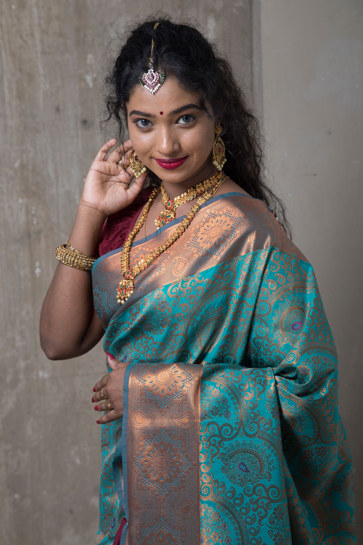 Model in a teal silk saree with a gold zari border and traditional jewellery