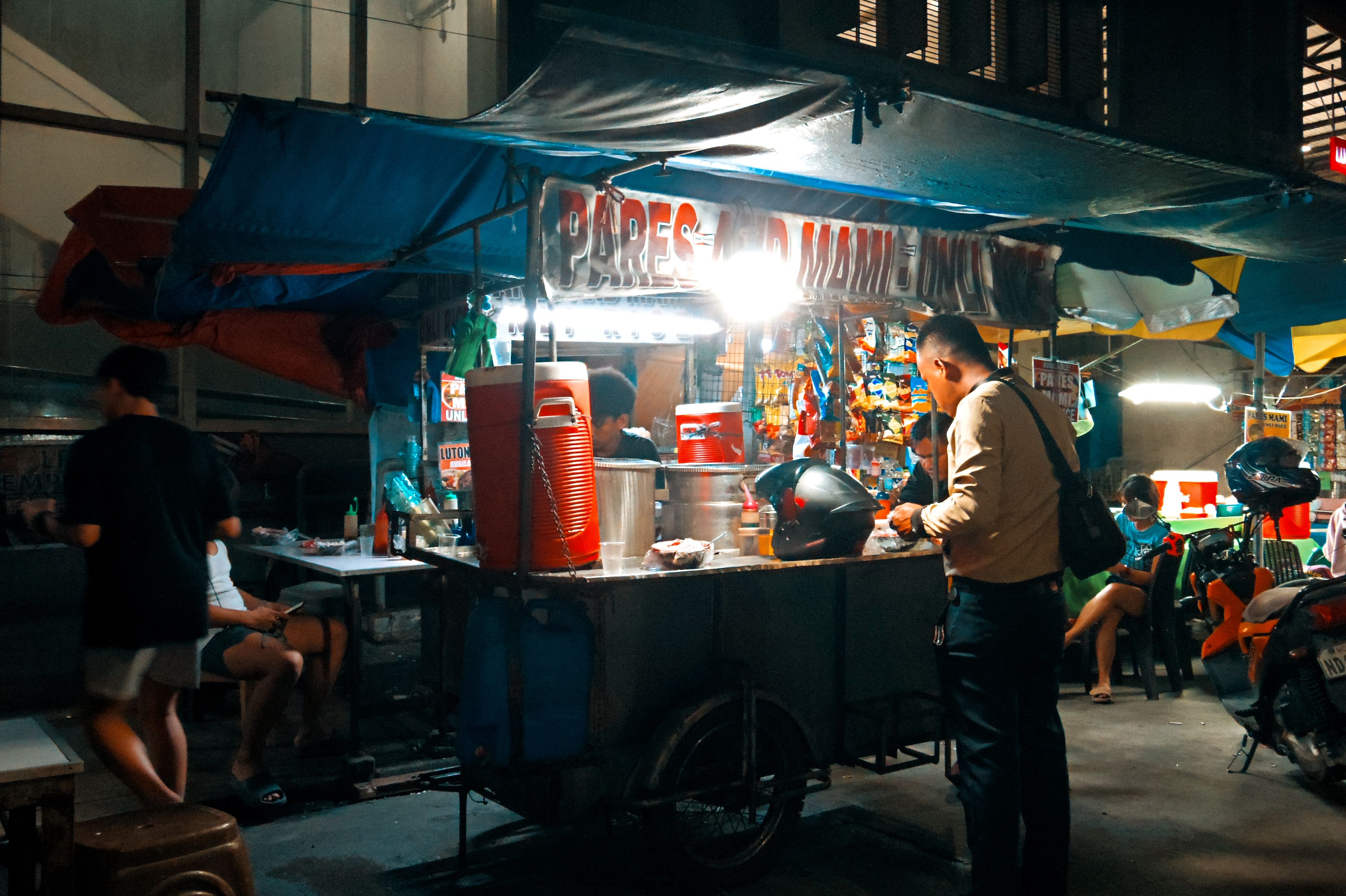 Busy night market food stall scene with people enjoying street food and vibrant atmosphere.