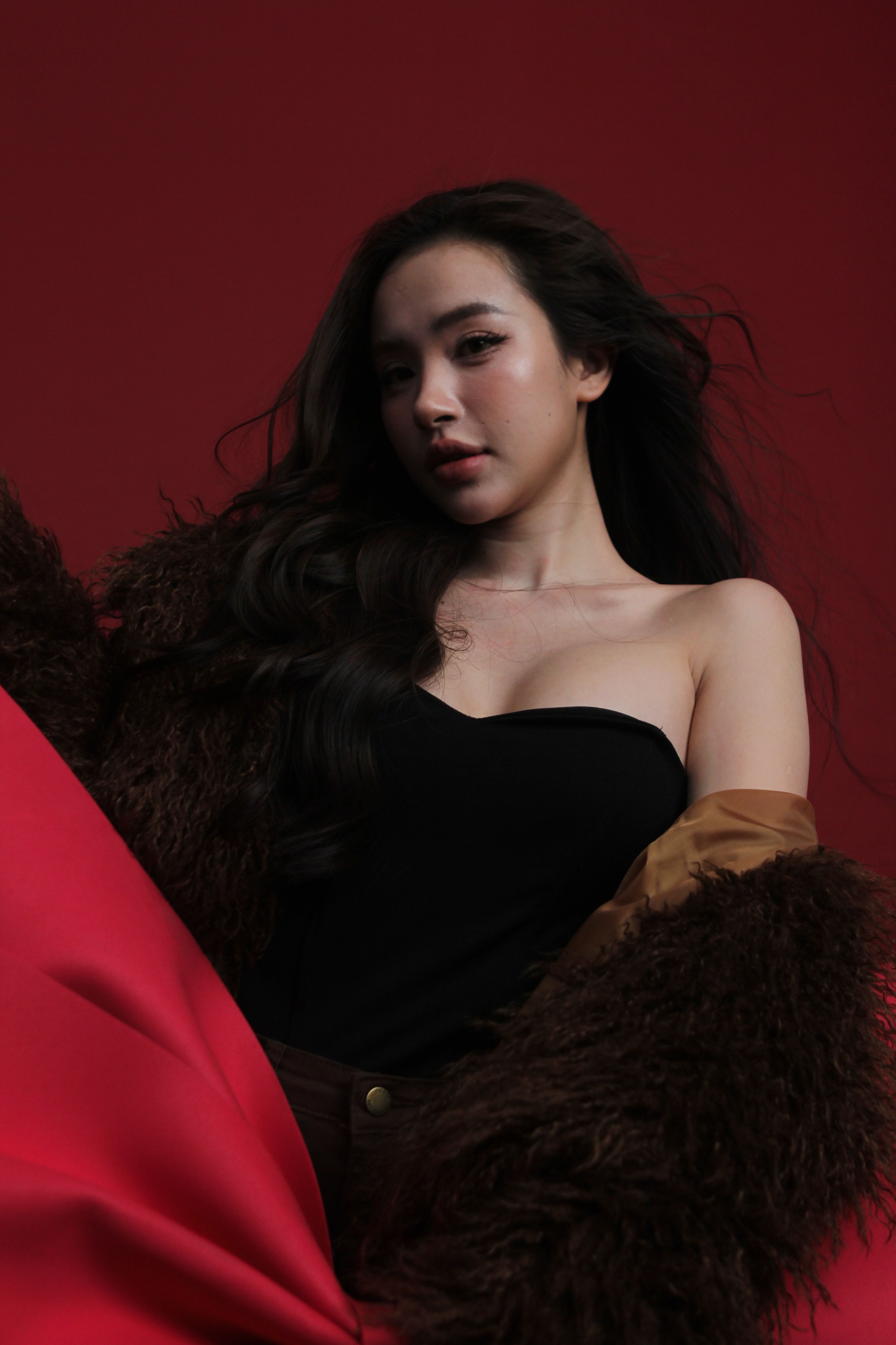 Stylish woman in fashionable fur and dress against a bold red backdrop. Perfect for fashion and lifestyle themes.