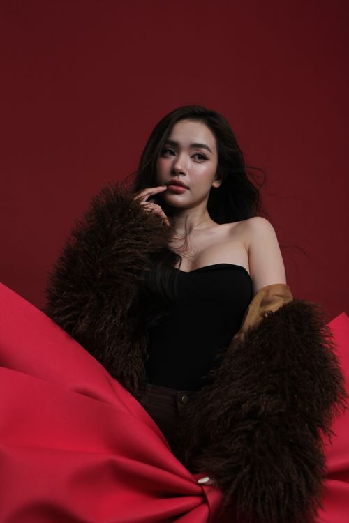 Free Elegant woman posing in fur coat and black outfit, set against a vibrant red backdrop. Stock Photo