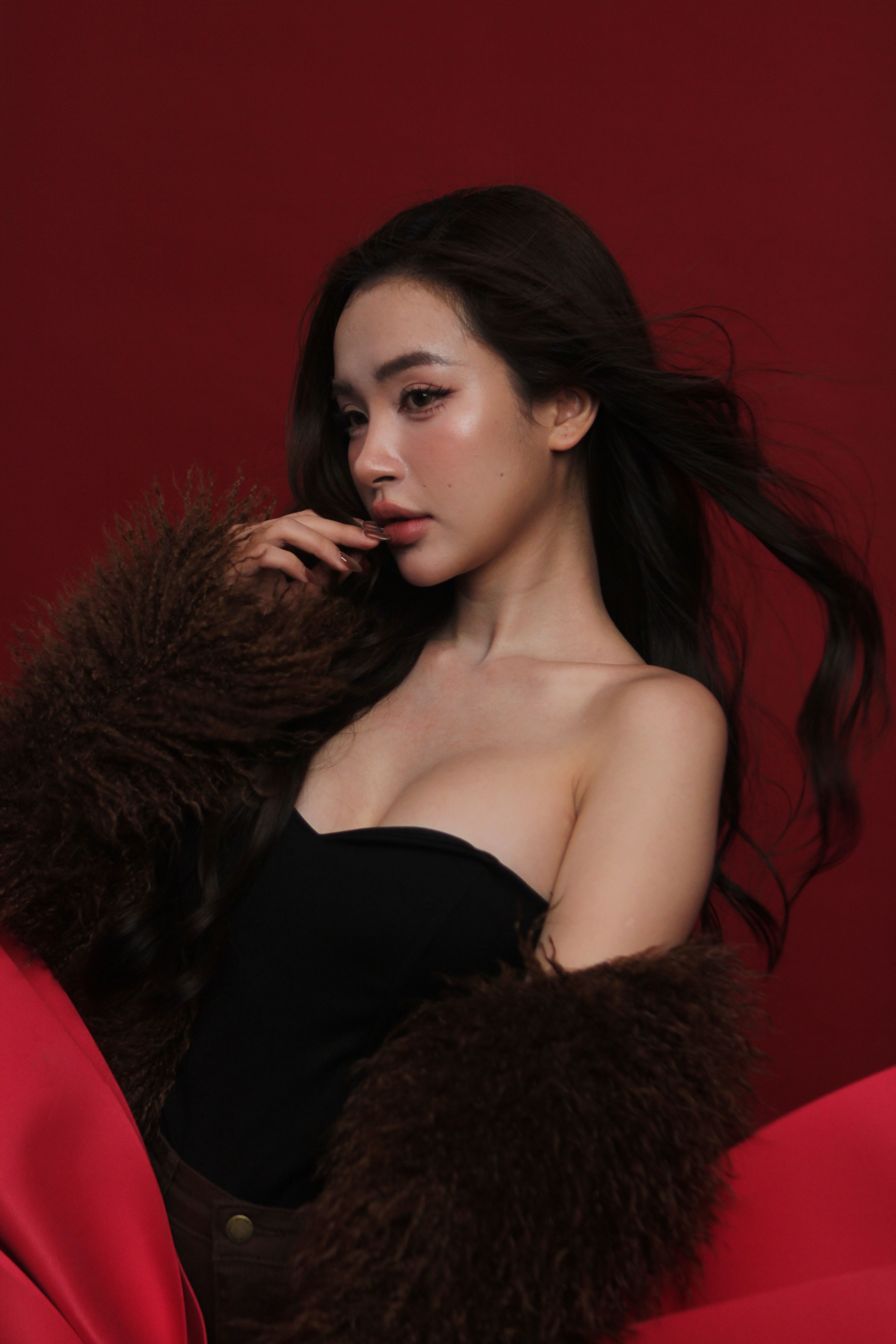 Elegant woman posing in dark fur coat with a red backdrop, showcasing fashion and style.