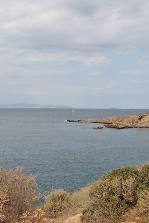Free Serene view of rocky coastline with sailboat in the distance under a partly cloudy sky. Stock Photo