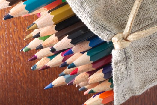 A collection of vibrant colored pencils spilling from a burlap bag on a wooden surface.