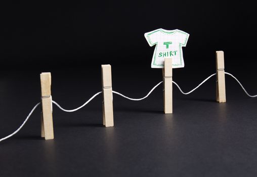 Artistic depiction of a paper t-shirt hung on a clothesline with wooden pins against a dark background.