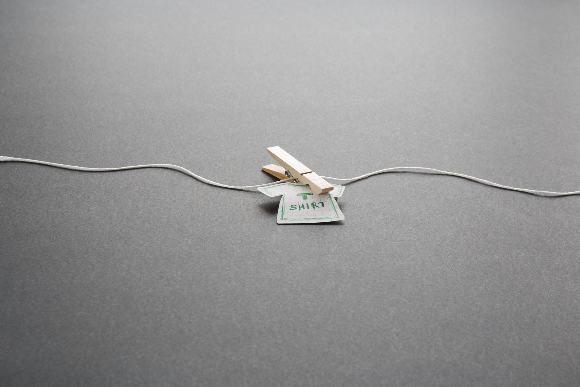 Simple paper shirt with clothespin on gray background, minimalist style.