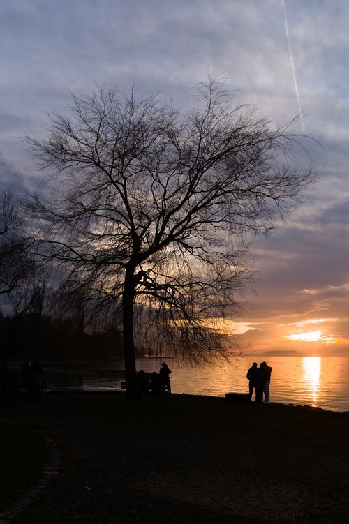 Free Silhouette of people by a serene lakeside at sunset. Dramatic sky and tranquil water scene. Stock Photo