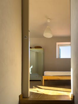 Simple minimalist bedroom with wooden bed and wardrobe, bathed in natural daylight.