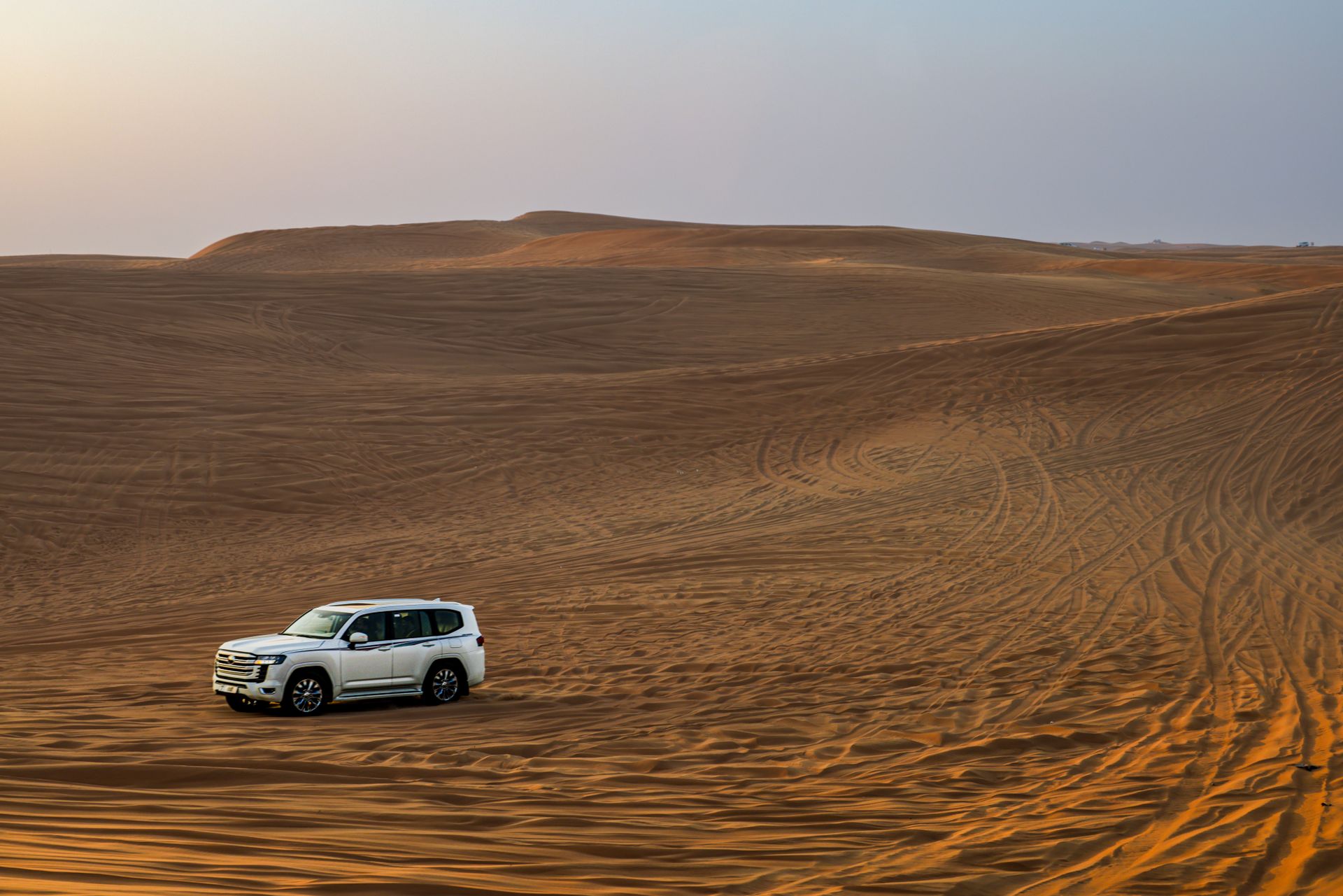 White SUV traversing expansive desert dunes at sunset, showcasing adventure and exploration.