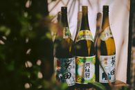 Three traditional Japanese sake bottles with distinctive labels in a natural setting.