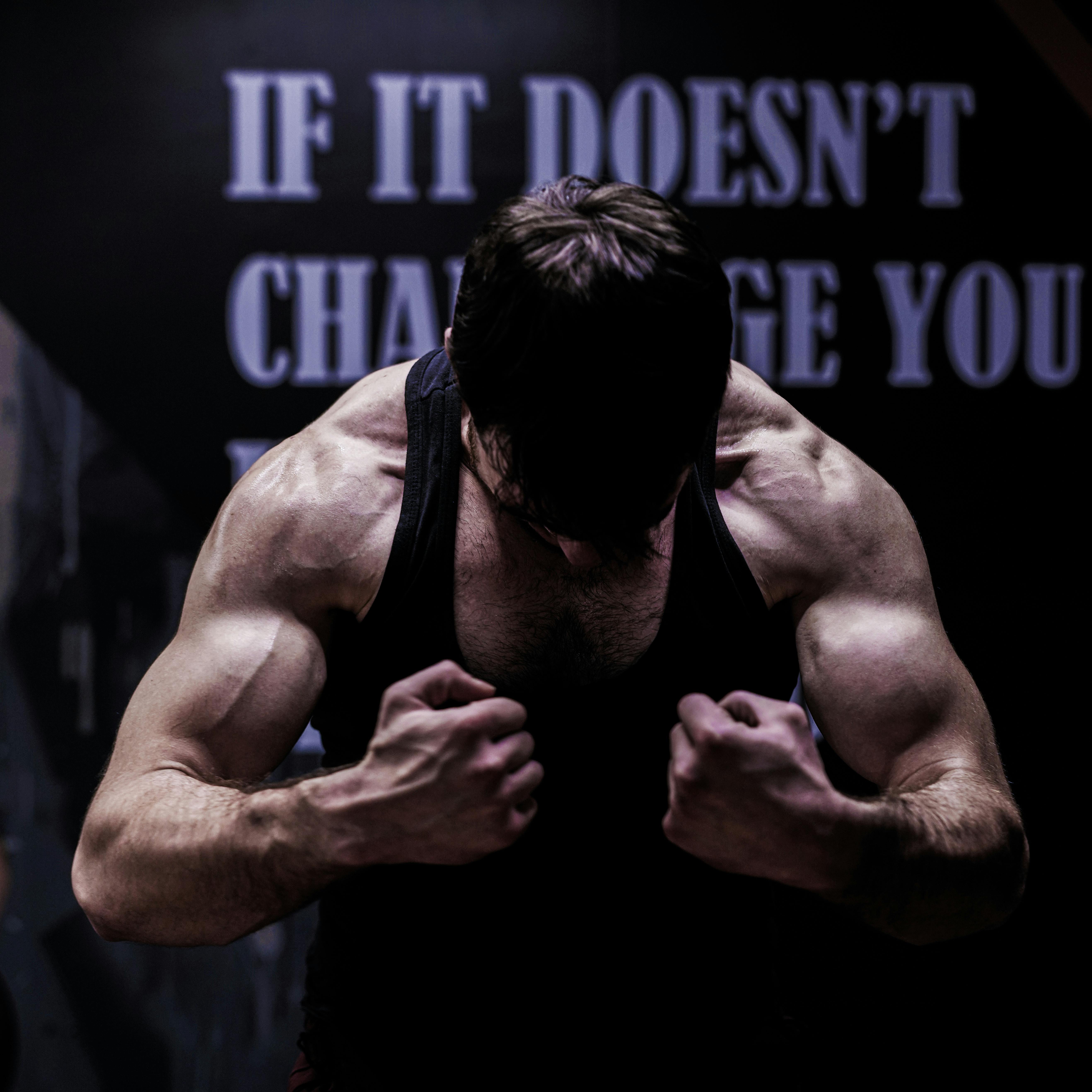 Muscular male bodybuilder posing in a dimly lit gym, showcasing strength and dedication.
