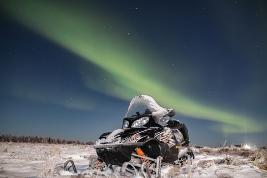Snowmobile parked in snowy landscape illuminated by Northern Lights at night.