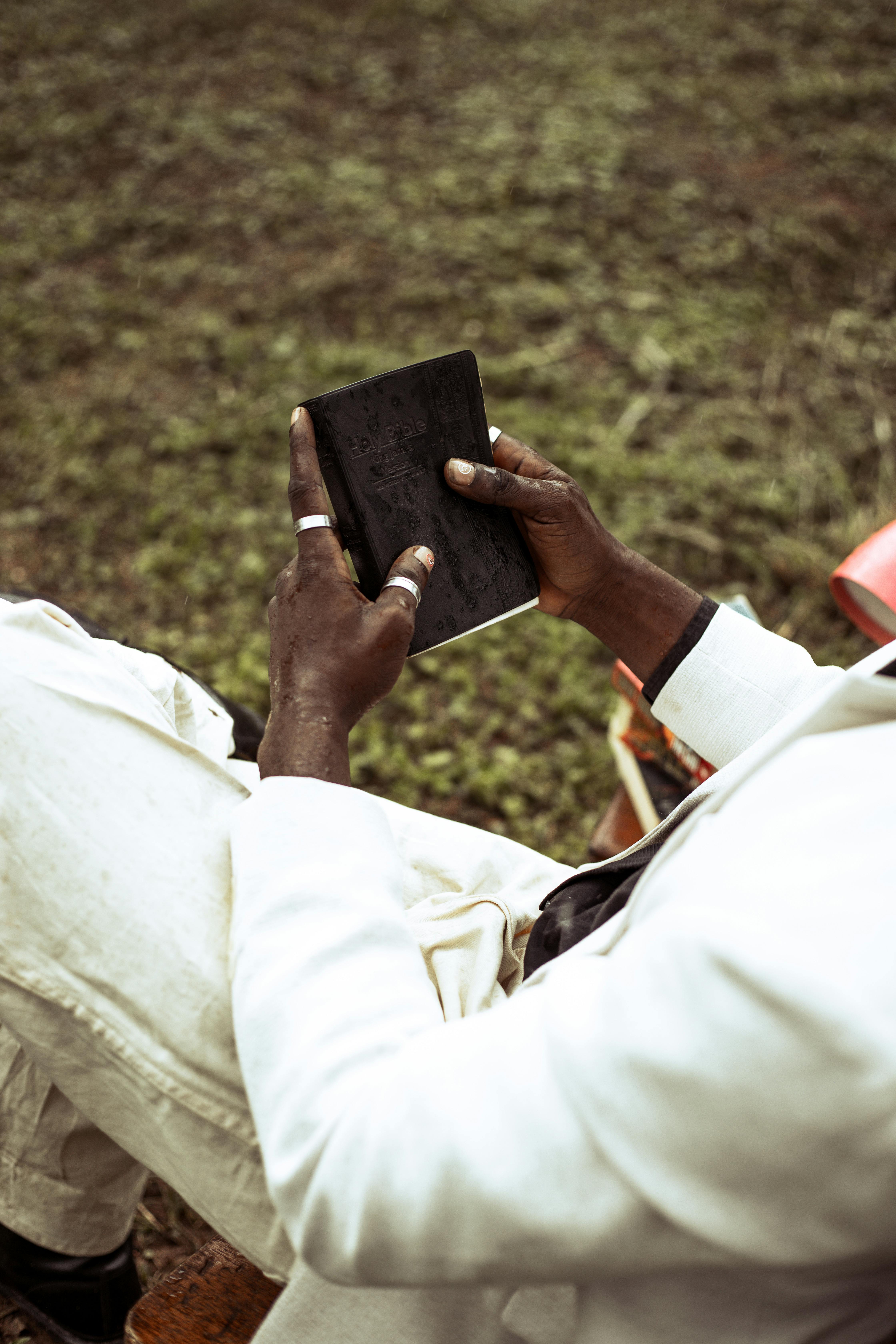 grátis Um homem vestindo um terno branco está sentado do lado de fora lendo um livro, criando uma atmosfera serena. Foto profissional