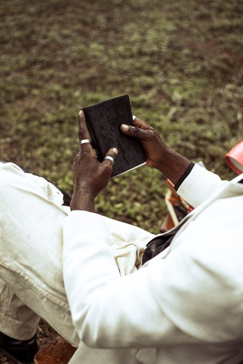 Free A man wearing a white suit sits outside while reading a book, creating a serene atmosphere. Stock Photo