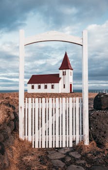 多云的天空下，一扇木制大门围起一座质朴的白色教堂，景色宁静