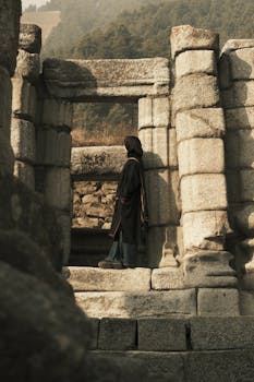 A woman stands in ancient stone ruins with natural lighting.