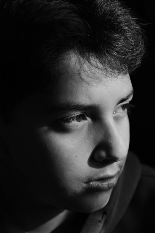Free Black and white close-up portrait of a thoughtful teenage boy looking away, in natural light. Stock Photo