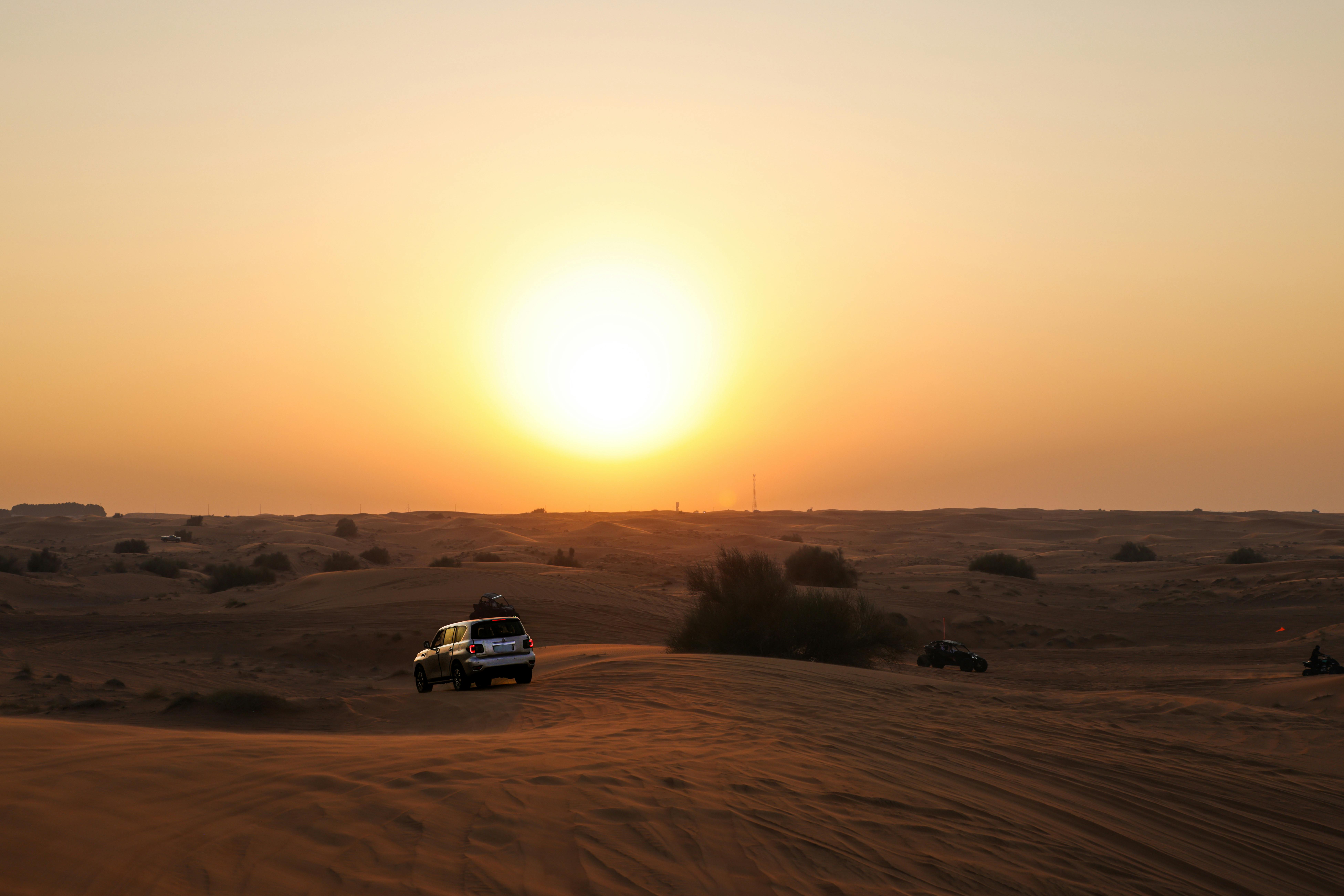 Stunning desert sunset with an SUV driving through sand dunes, capturing adventure and serenity.