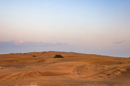 A scenic view of a desert landscape at sunset with 4x4 vehicles and sand dunes.