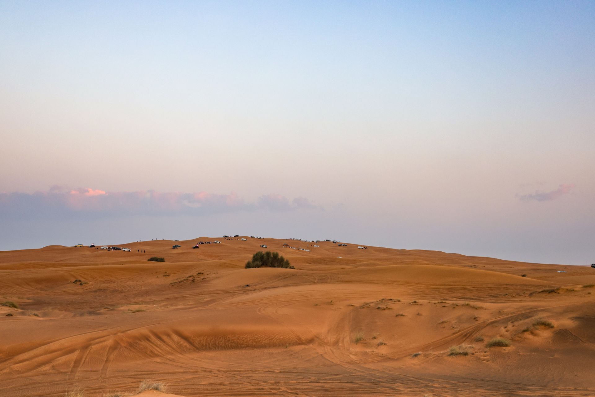 A scenic view of a desert landscape at sunset with 4x4 vehicles and sand dunes.