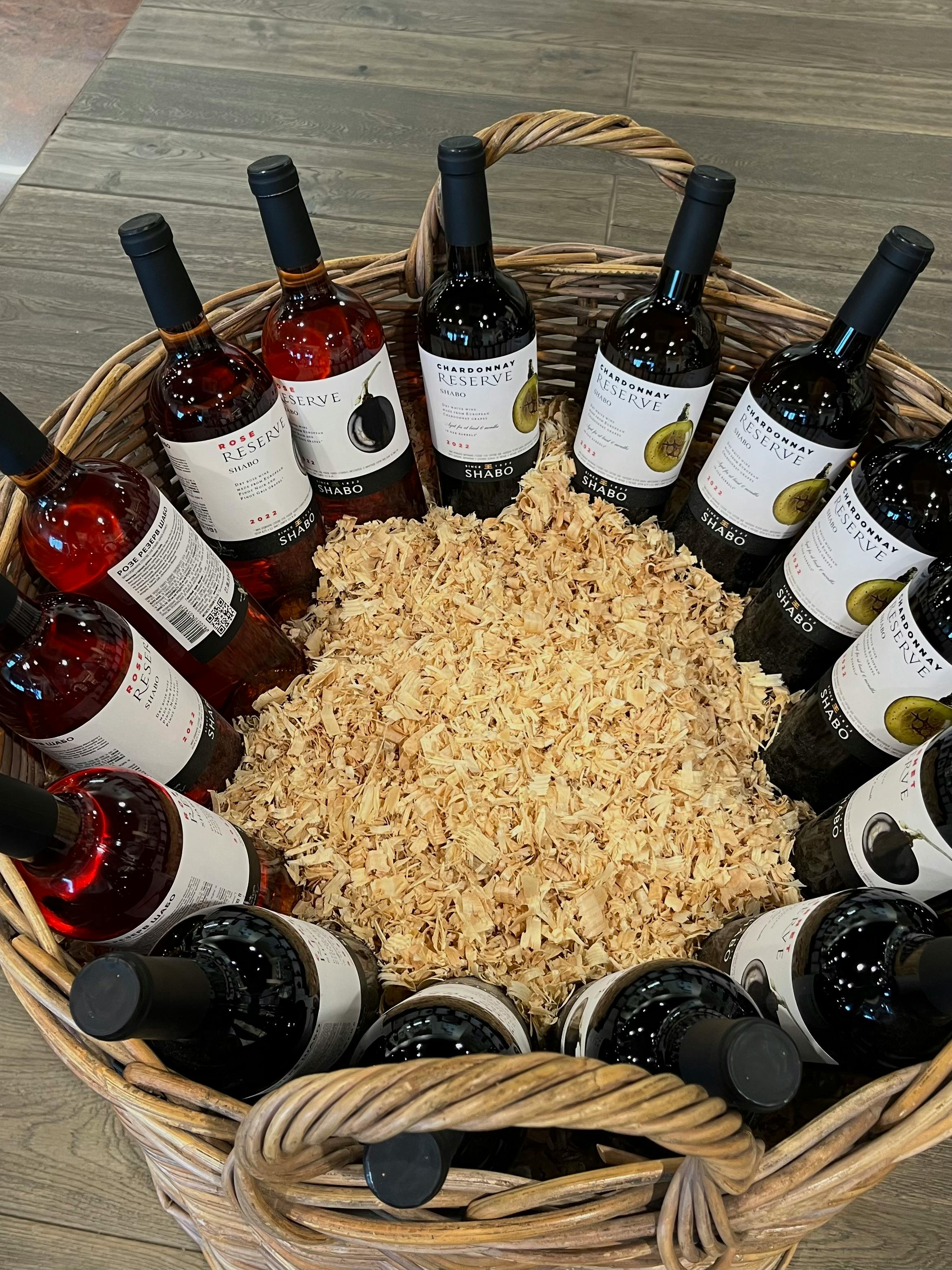 A diverse collection of wine bottles arranged in a wicker basket, surrounded by wood shavings.