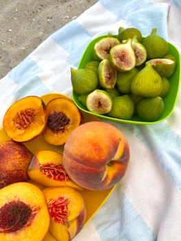 Sliced peaches and fresh figs on a colorful towel, creating a summer picnic vibe.