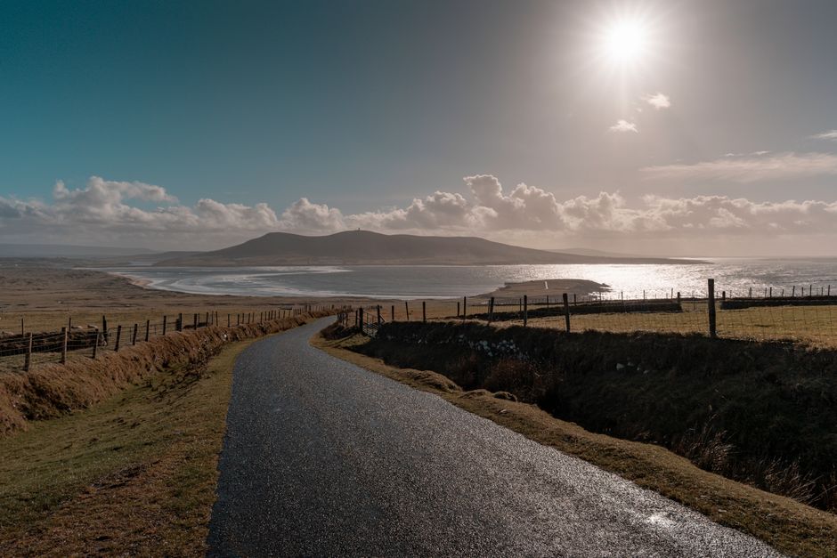A picturesque coastal road in Ireland with rolling hills and ocean views under a bright sun. A picturesque coastal road in Ireland with rolling hills and ocean views under a bright sun.